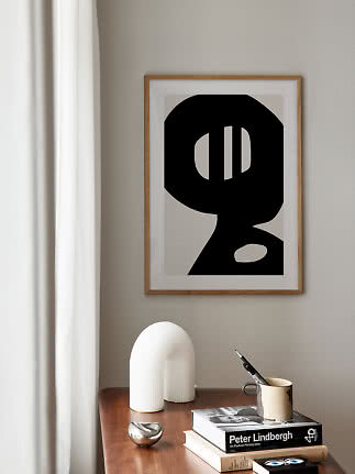 Gerahmtes abstraktes Schwarz-Weiß-Poster über einem Holztisch mit Büchern, Tasse und weißer Skulptur.