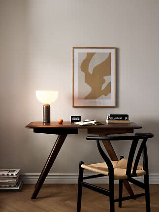 Dark wooden desk with black chair, lit table lamp and abstract wall art