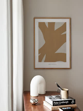 Abstracte beige poster in houten lijst boven een houten tafel met boeken, mok en witte decoratie