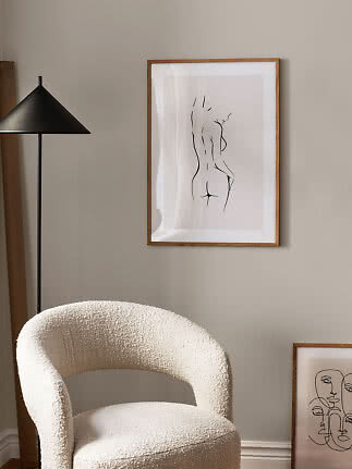 Bouclé armchair beside black floor lamp and framed line art on a beige wall
