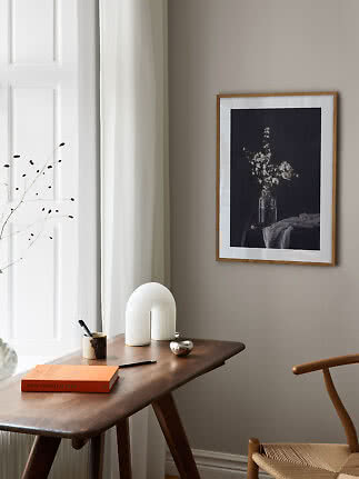 Holzgerahmter Blumenprint an beigefarbener Wand über dunklem Holzschreibtisch am Fenster