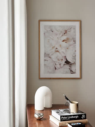 Ramme med lyst blomsterprint over et træbord med bøger, vase og krus ved et vindue