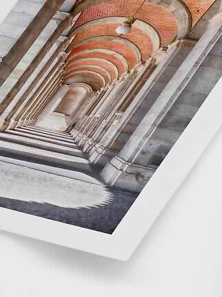 Photograph of a colonnade with stone arches, brick ceiling and hanging lamp