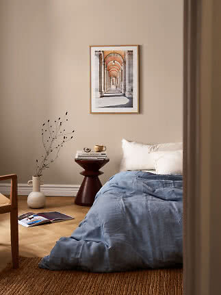 Cozy bedroom with blue duvet, side table, vase, and framed architectural print on a beige wall
