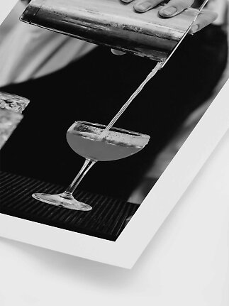 Sort-hvidt foto af drink, der hældes fra shaker i margaritaglas med saltkant