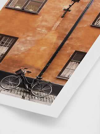 Schwarzes Fahrrad vor orangefarbener Hauswand mit Fenstern und Kopfsteinpflaster