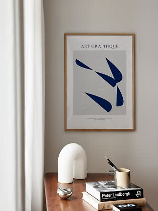 Framed abstract blue art print above a wooden table with books and decorative objects