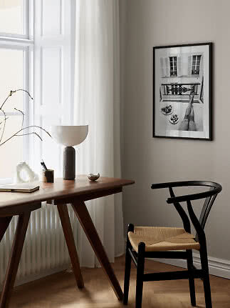 Minimalistische Ecke mit Holztisch, schwarzem Stuhl, Tischlampe und gerahmtem Schwarzweißfoto.