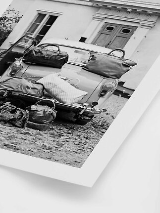 Sort-hvid foto af veteranbil med flere tasker stablet bagpå foran en bygning
