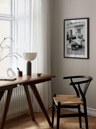 Minimalistisk hjemmekontor med træbord, sort stol og indrammet sort-hvid plakat på væggen