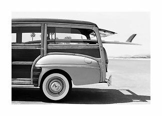 Foto em preto e branco de uma perua vintage com prancha de surf na lateral junto à estrada costeira