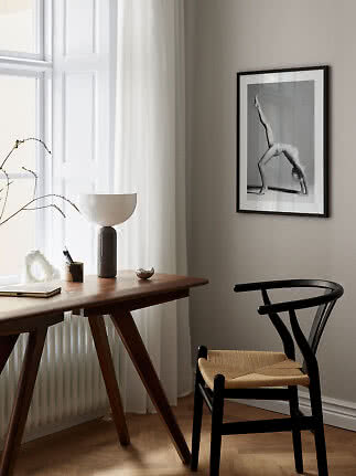 Minimalist workspace with wooden desk, black chair, table lamp and framed black-and-white wall art