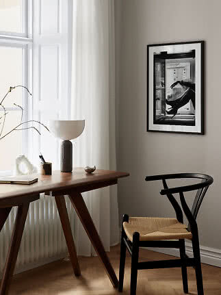 Minimalistisk hjemmekontor med træbord, sort stol, lampe og indrammet sort-hvid foto ved vindue