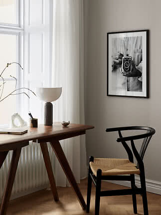 Angolo studio minimalista con scrivania in legno, sedia nera, lampada e foto in bianco e nero.