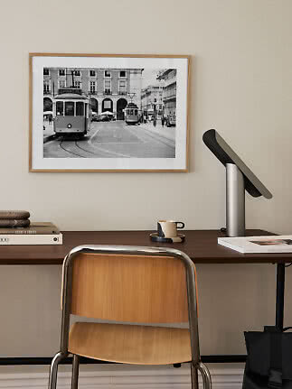 Skrivebord med stol, lampe og indrammet sort-hvid foto af sporvogne på beige væg
