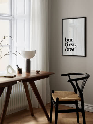 Framed typographic print reading "but first, love" above a wooden desk and black chair