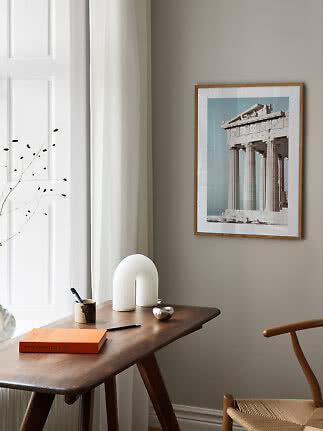 Framed print of a classical temple above a wooden desk by a window