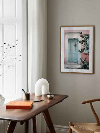 Framed photo of a mint green door on a beige wall above a wooden table by a window