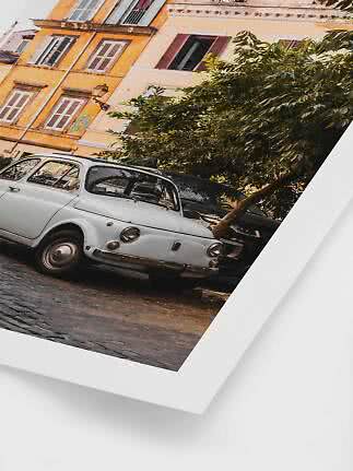 Classic white car parked on a cobblestone street by colorful buildings and trees