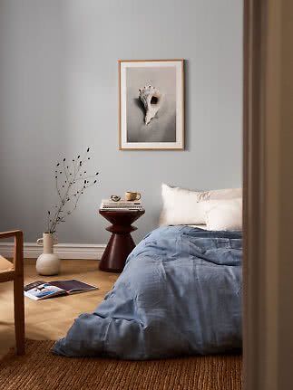 Bedroom with blue bedding and framed seashell print on a gray wall