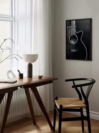 Black framed guitar wall art above a wooden desk with lamp and black chair