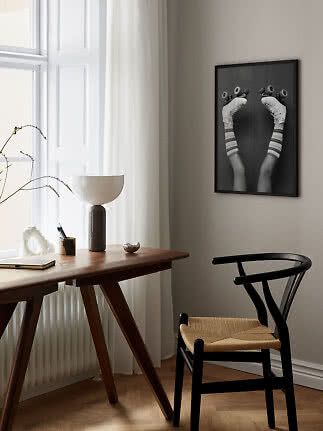 Schwarz gerahmtes Poster mit Beinen auf Rollschuhen über einem Holztisch im hellen Raum