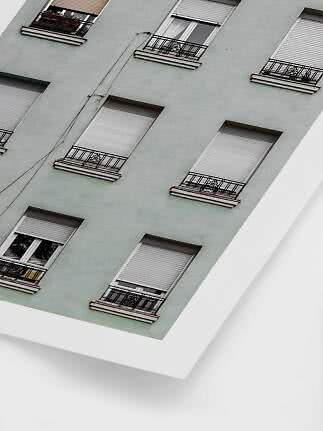Angled photo of an apartment building facade with several windows, shutters and black railings