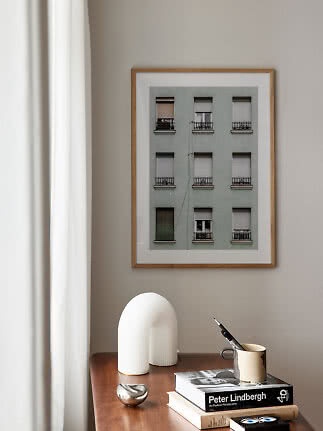 Framed building photo on a beige wall above a wooden table with books, mug and white sculpture