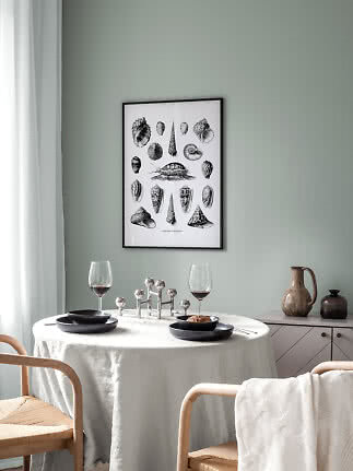 Framed black-and-white shell print above a set dining table in a calm, light room
