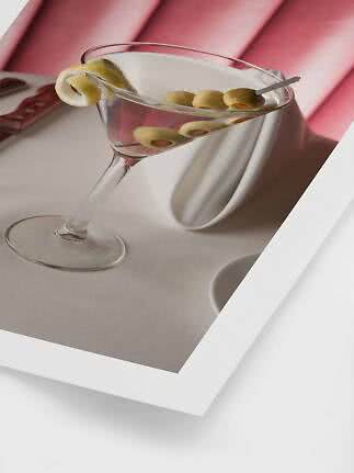 Martiniglas mit klarem Drink, grünen Oliven und Zitronenzeste auf weißer Tischdecke