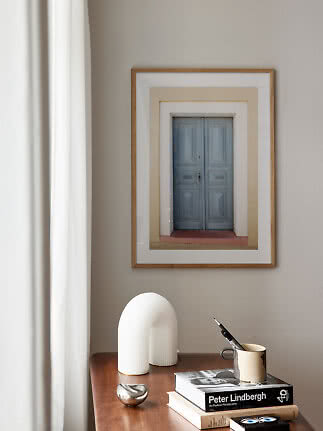 Framed print of a blue double door on a beige wall above a wooden table with books and decor
