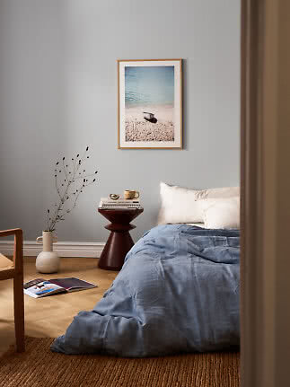 Bedroom with blue duvet, side table and framed beach print on a gray wall