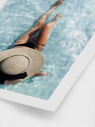 Person in a black swimsuit and large straw hat floating in a light blue pool