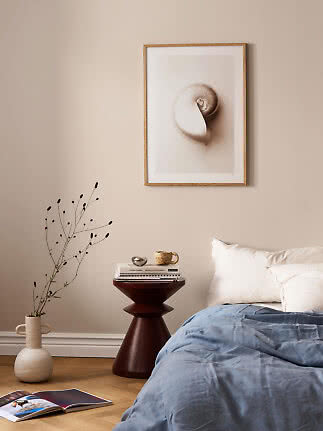 Shell print in a light wood frame above a bed and side table in a calm bedroom