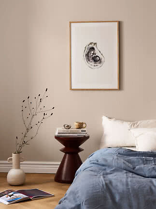 Bedroom with framed oyster artwork above bed, blue duvet, side table and floor vase