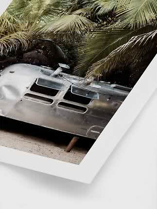 Silver trailer on sand beneath palm leaves, shown as a framed print
