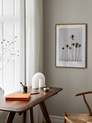 Gerahmter Palmenprint an der Wand über einem Holztisch am hellen Fenster