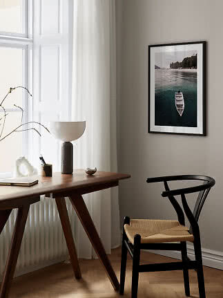 Framed photo of a boat on calm water hanging above a desk in a bright room.