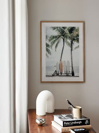 Framed beach print with palm trees and surfboards above a wooden table with books and decor