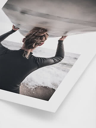 Person in a black wetsuit lifting a surfboard by the beach, viewed from behind