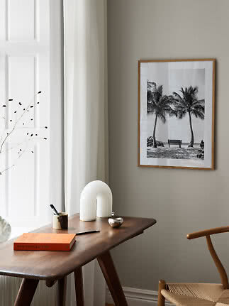Framed black-and-white palm tree print above a wooden desk in a bright minimalist room