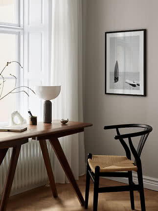 Minimalistisk arbejdsplads med træskrivebord, sort stol, bordlampe og indrammet surf-foto på væggen