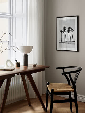 Minimalist home office with wooden desk, black chair, table lamp and framed palm tree print