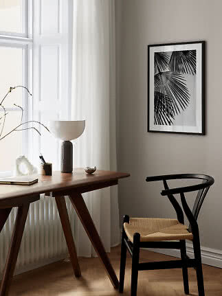 Black framed palm leaf print hanging above a wooden desk by a bright window.