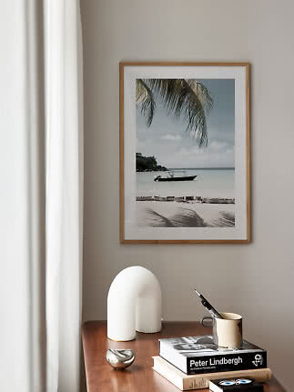Framed beach print with boat and palm above a wooden table with books and decor