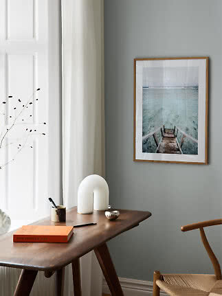 Framed wall art of stairs into turquoise sea above a wooden desk in a bright room