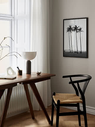Black framed palm tree print above a wooden desk and black chair by a bright window