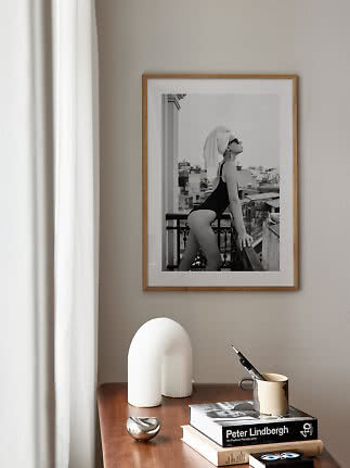 Framed black-and-white photo print above a wooden table with books, mug and white decor
