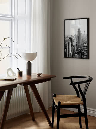 Sort indrammet plakat med New York-skyline over et skrivebord i et lyst, moderne rum