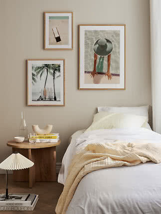 Sovrum med vit säng, träbord och tre inramade strandmotiv på beige vägg